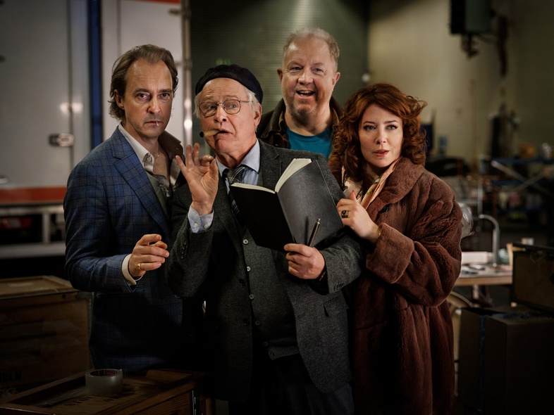 Fyra vuxna personer står tillsammans inomhus, en håller en anteckningsbok och penna, alla tittar mot kameran.