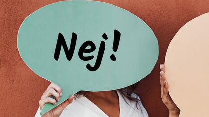 Person håller upp en pratbubbla med texten 'Nej!' framför ansiktet mot en röd vägg.