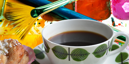En kopp kaffe, en bulle, två penslar och en färgpalett med vattenfärger i starka färger.