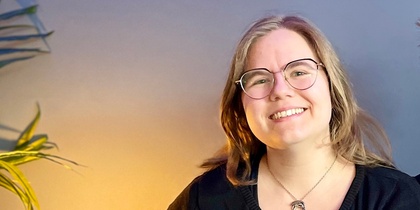 Två leende personer sitter tillsammans i en blå soffa i ett rum med blå vägg och grön växt.