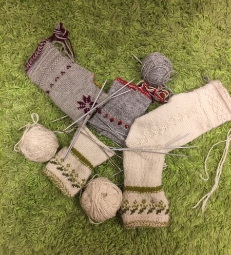 Två par stickade sockor under arbete med garnnystan och stickor på en grön matta.