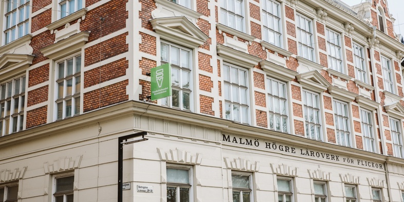 Fasad av en gammal tegel- och putsbyggnad med stora fönster och skylten 'Malmö högre läroverk'.