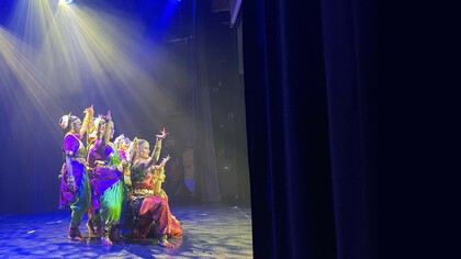 Grupp av dansare i färgglada traditionella kläder på scen med dramatiskt ljus.