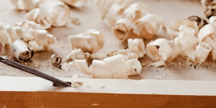 En person arbetar med träbearbetning, använder en mejsel och hammare på en träplanka.