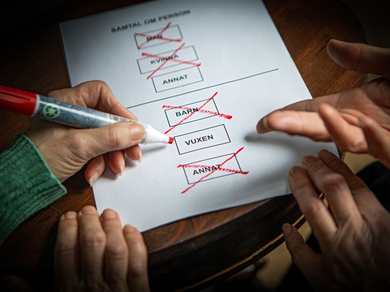 Två händer markerar och kryssar i rutor på ett formulär för bildstöd med en röd penna.