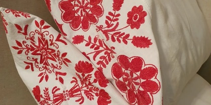 Två vita kuddar med rött, blommigt broderimönster ligger mot en beige bakgrund.