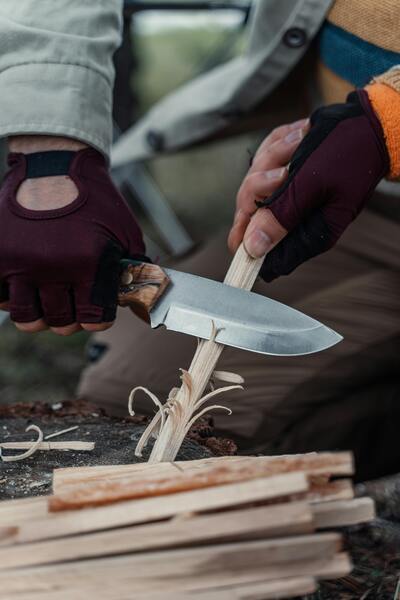 En person täljer trä med en stor kniv, händer med handskar syns tydligt.
