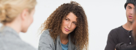 Kvinna med lockigt hår lyssnar uppmärksamt på en annan person i en gruppdiskussion.