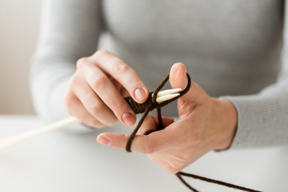 Närbild på händer som stickar med bruna garntrådar och vita stickor.