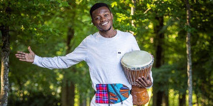 En leende man står barfota på en trästig i skogen och håller en trumma under armen.