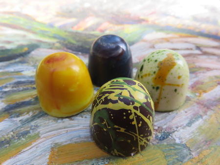 Fyra färgglada praliner med konstnärliga mönster ligger på en målad yta.