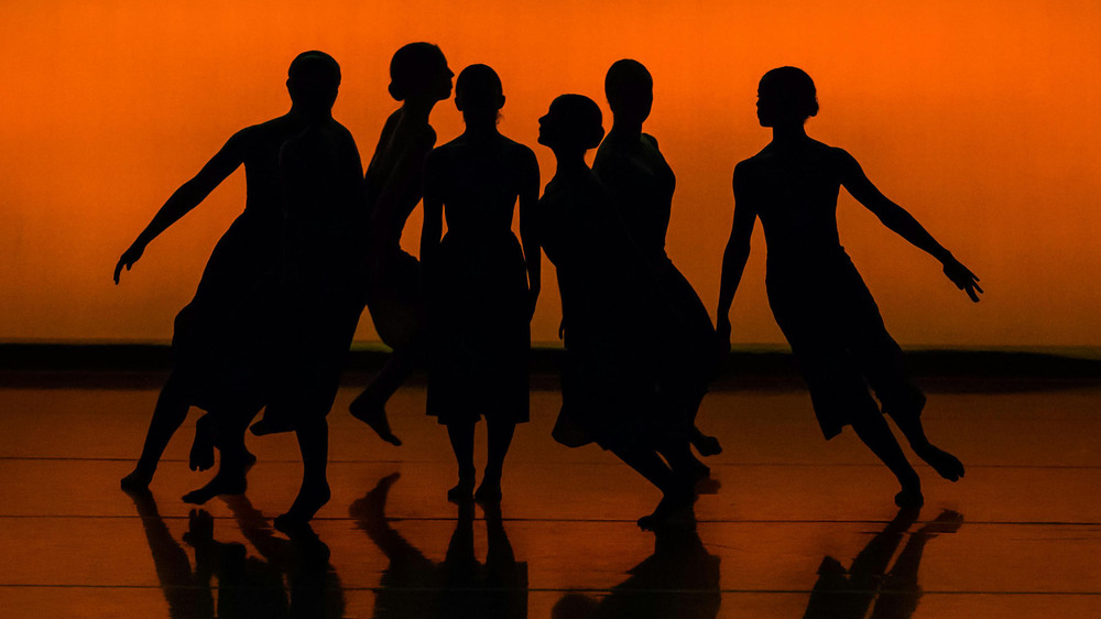 Sex dansare i silhuett mot en orange bakgrund, poserar tillsammans på scenen.