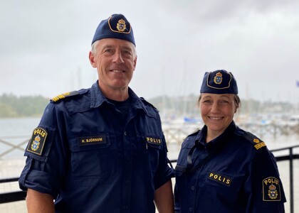 Två svenska poliser i uniform står utomhus vid en hamn med båtar i bakgrunden.