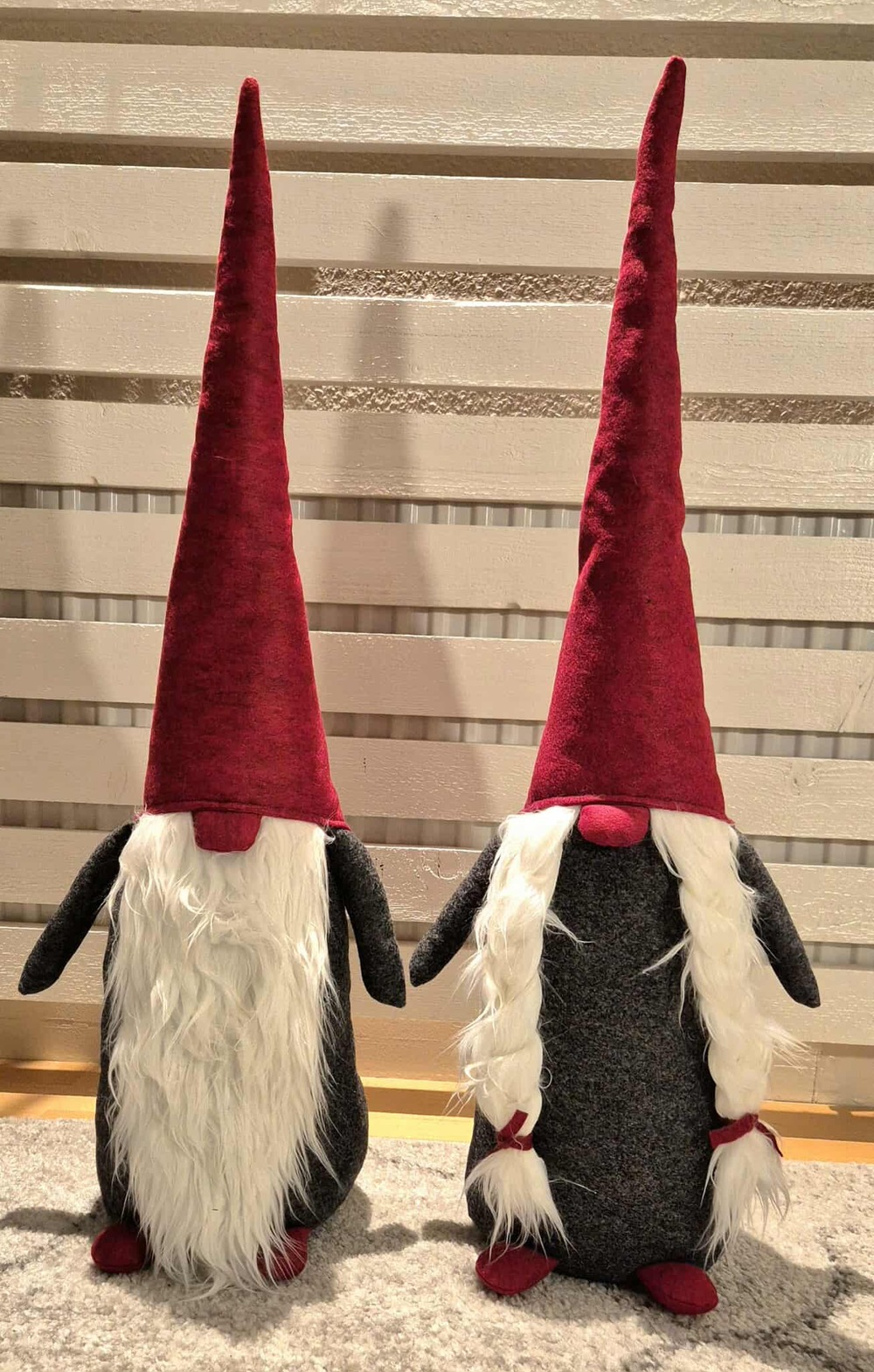 Två tomtenissar med långa röda luvor och vita skägg står bredvid varandra på en matta.