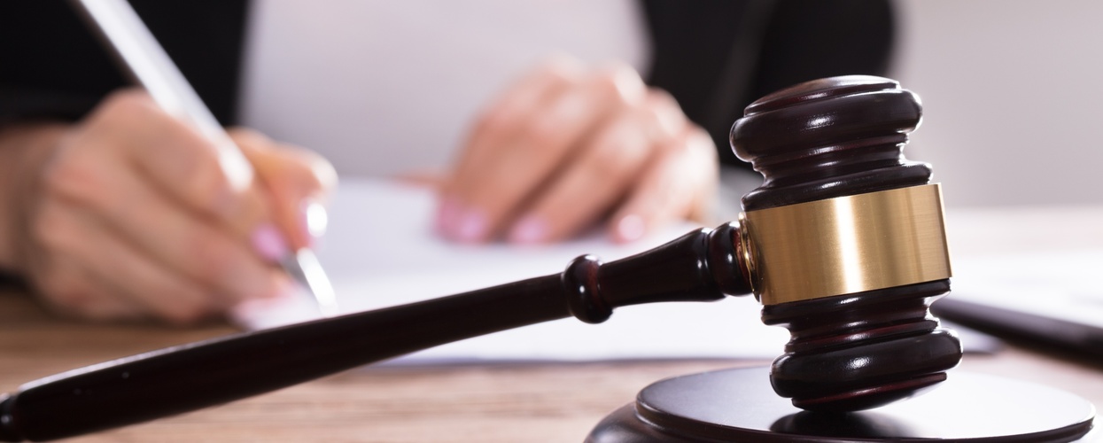 En domarklubba ligger på ett skrivbord medan en person skriver på papper i bakgrunden.