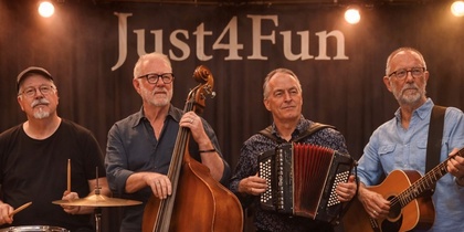 Fyra musiker spelar på scen med trummor, kontrabas, dragspel och gitarr inför en applåderande publik.