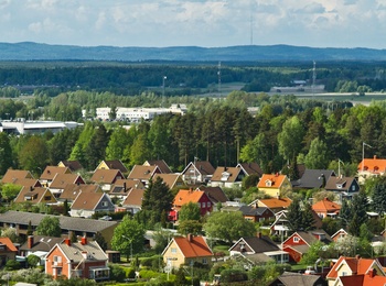 Färgglada villor med röda och gula tak i ett lummigt bostadsområde, omgivna av skog och berg i bakgrunden.