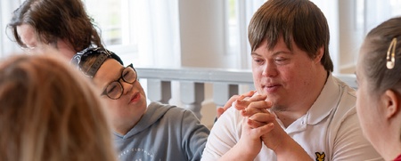 Fyra personer sitter runt ett bord och samtalar. Text om tillgänglighet för alla syns i bilden.