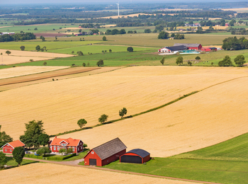 Landskapsvy över åkrar och bondgårdar med röda hus och lador på den svenska landsbygden.
