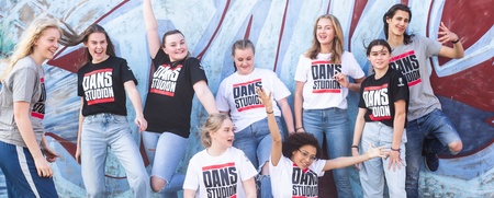 En grupp unga personer poserar glatt framför en graffitivägg, alla bär t-shirts med texten 'DANS STUDION'.