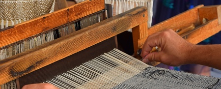 Närbild av händer som väver tyg på en traditionell vävstol.