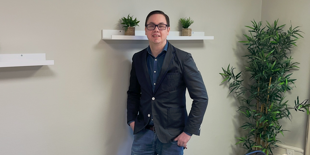 En person står vid väggen i ett mötesrum med bord, stolar, växter och hyllor med krukväxter.