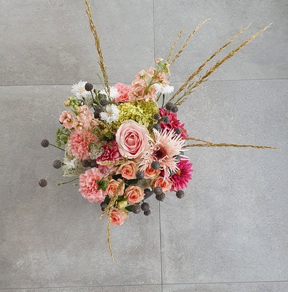En bukett med rosa, vita och röda blommor samt torkade gräs på ett grått klinkergolv.
