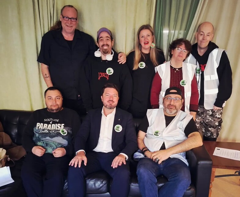 Gruppfoto av åtta personer, några sitter i soffa och andra står bakom, alla har ansikten suddade.