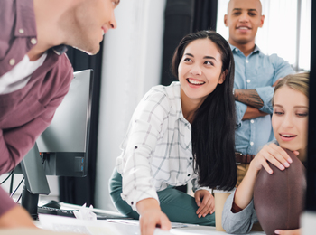 Fyra unga vuxna samarbetar och diskuterar vid ett skrivbord på ett modernt kontor.