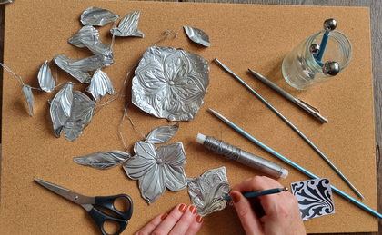 En person arbetar med metallprägling och formar blommor och blad av tunn metall på en korkmatta.