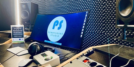 Ett modernt ljudinspelningsstudio med dator, högtalare, hörlurar och ljudutrustning på ett skrivbord.