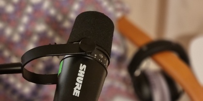 En svart Shure-mikrofon på stativ med hörlurar på en stol i bakgrunden.