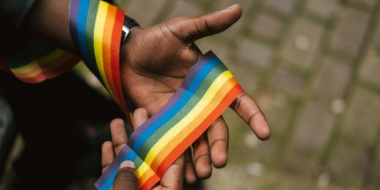 Två händer håller ett regnbågsfärgat band, symbol för HBTQ+-rörelsen.