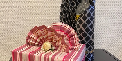 Två inslagna presenter på ett svart bord, en i randigt papper med rosett och en flaska i mönstrat papper.