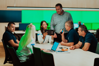 En grupp människor sitter runt ett konferensbord och diskuterar med laptops och surfplattor.