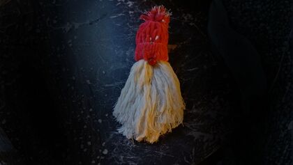 En handgjord tofsfigur med röd mössa och vit kropp ligger på en mörk yta.