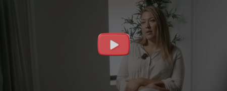 En person sitter i en ljus inomhusmiljö med en mikrofon på skjortan, växter syns i bakgrunden.