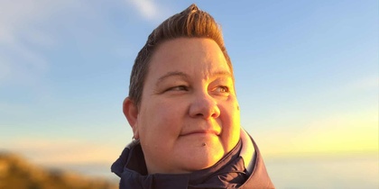 Person i mörk jacka står utomhus i solnedgång, ansiktet är suddat för anonymitet.