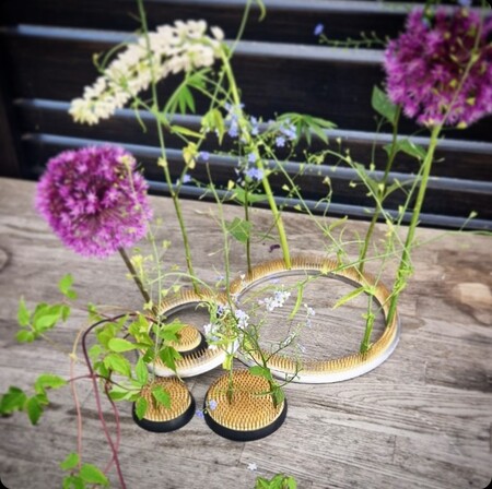 Olika blommor arrangerade i små runda blomsterhållare på ett träbord utomhus.