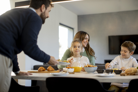 En familj sitter vid ett matbord och äter frukost tillsammans i ett modernt kök.