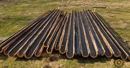 Långa urholkade trädstammar ligger på gräsmark, troligen för att användas som takrännor eller vattenrännor.