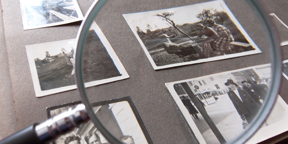 Ett fotoalbum med svartvita fotografier granskas med ett förstoringsglas.