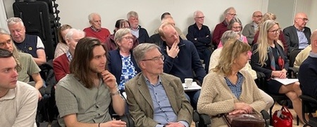 En grupp vuxna sitter i ett konferensrum och lyssnar på en presentation eller föreläsning.