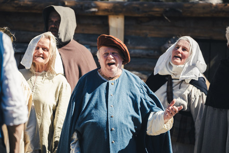 En grupp människor i historiska kläder står utomhus framför en träbyggnad.