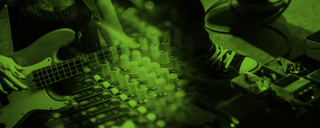 En person spelar elbas bredvid ett mixerbord och effektpedaler, bilden har ett grönt filter.