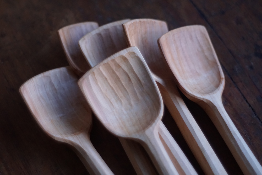 Sex handgjorda träslevar ligger samlade på ett mörkt träbord.