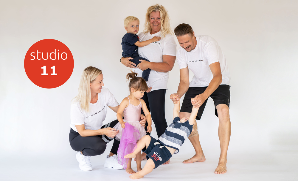 Fem personer, två vuxna och tre barn, leker tillsammans i en ljus fotostudio med vit bakgrund. En röd cirkel med texten 'studio 11'.