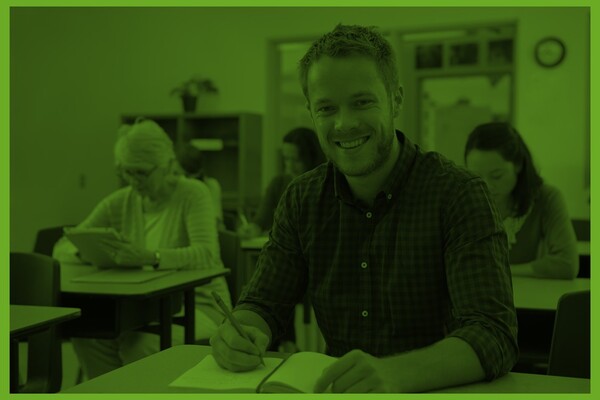 Vuxna personer sitter vid skolbänkar i ett klassrum.