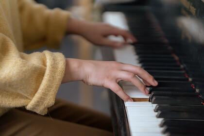 Närbild på händer som spelar på ett piano, personen bär en gul tröja.
