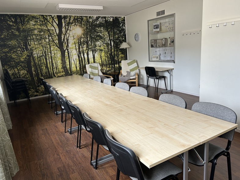 Ett mötesrum med långbord, stolar, fåtöljer och en vägg med skogsmotiv.
